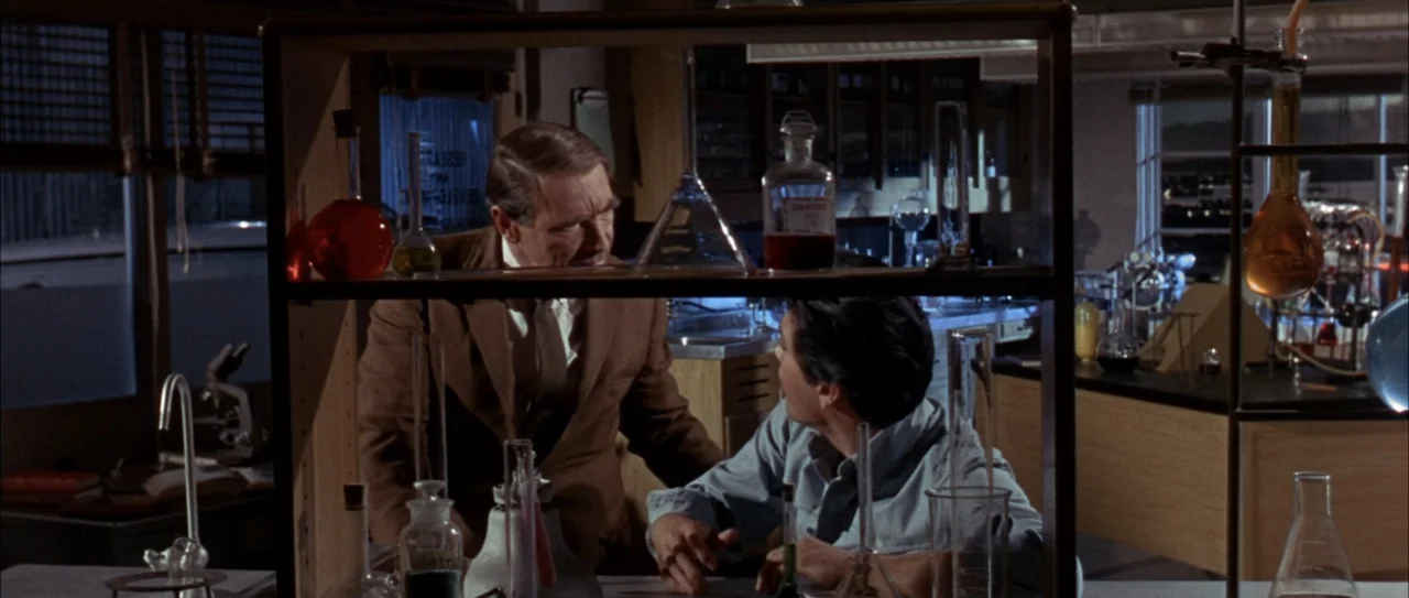 Clambake (1967) movie still: medium — A 1950s laboratory interior features wooden shelves packed with various colorful glass chemical vessels. An…