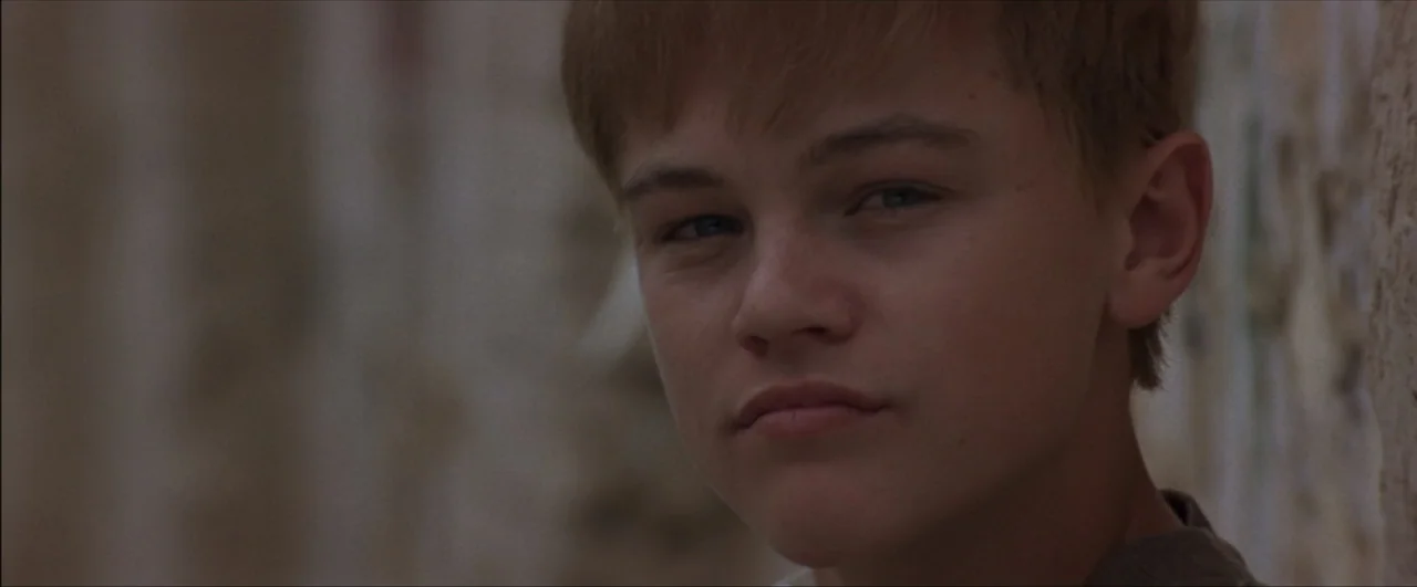 This Boy's Life (1993) movie still: closeup — A close view of a teenage boy standing against a textured stone wall. The boy looks directly at the…