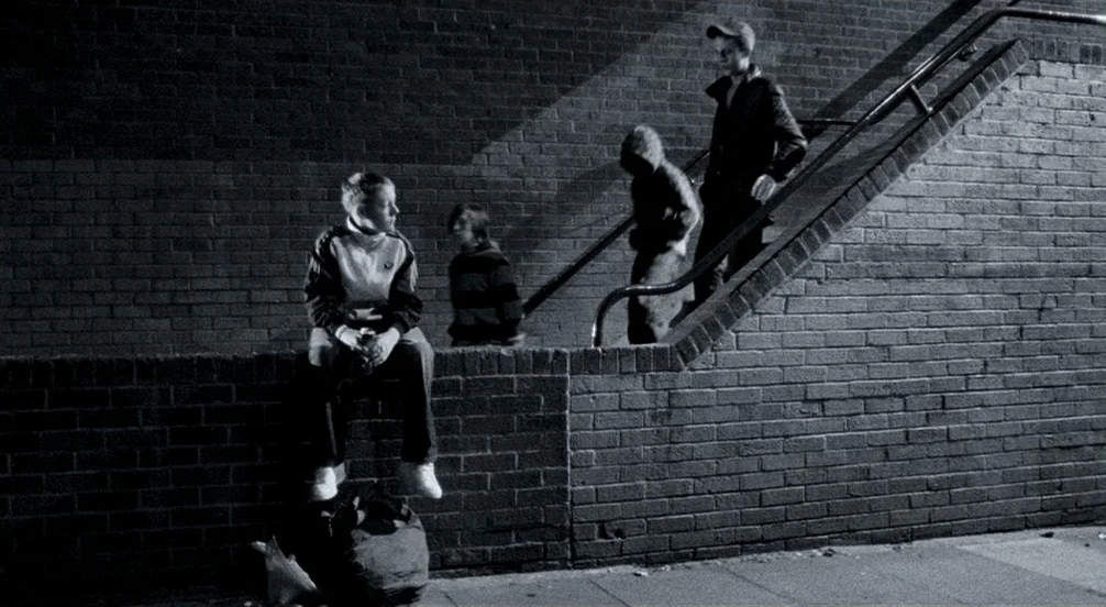 Somers Town (2008) movie still: fullbody — A dark brick underpass features a wall and staircase illuminated by overhead street lighting. Three…