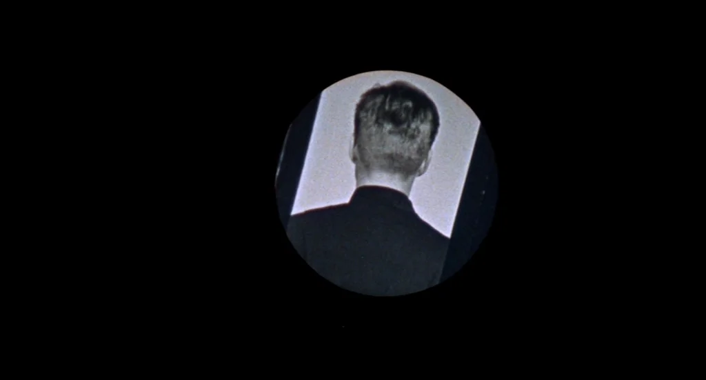 Fahrenheit 451 (1966) movie still: closeup — A circular projection frame shows the back of a man in a dark suit. The subject remains static while…