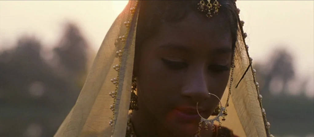 Brick Lane (2007) movie still: closeup — A woman stands outdoors in soft light with a blurred natural landscape behind her. She wears a golden veil…