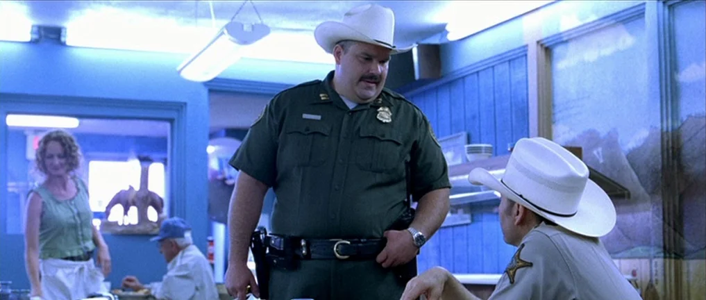 The Three Burials of Melquiades Estrada (2005) movie still: medium — A diner interior features blue paneled walls and a landscape mural on the wall.…