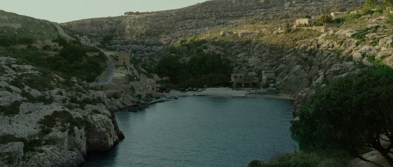 By The Sea (2015) movie still: establishing — A deep rocky cove with limestone cliffs surrounding a small tranquil body of water. Sparse greenery…