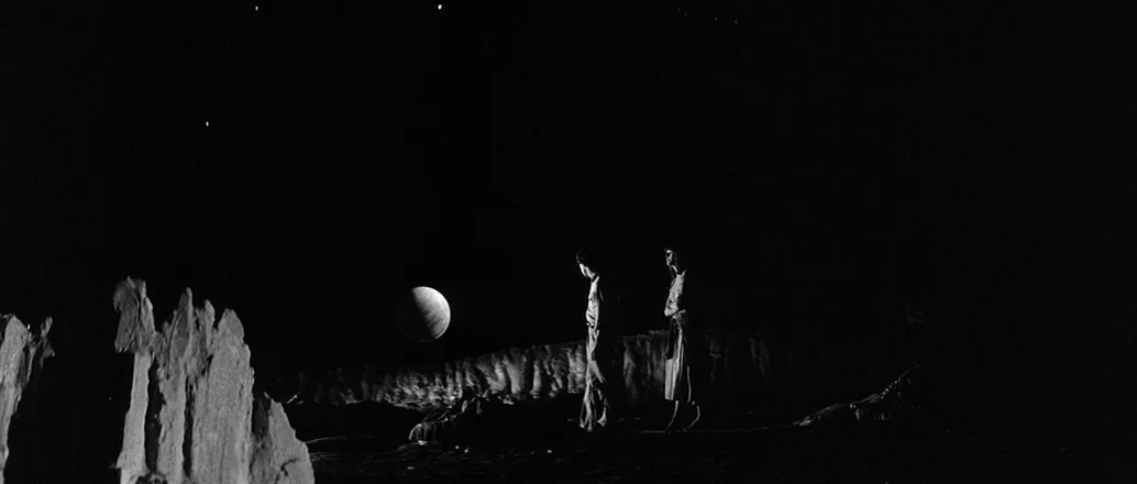 Manhattan (1979) movie still: wide — A desolate alien rocky terrain under a dark night sky with distant stars. Two people stand on the dark ground…
