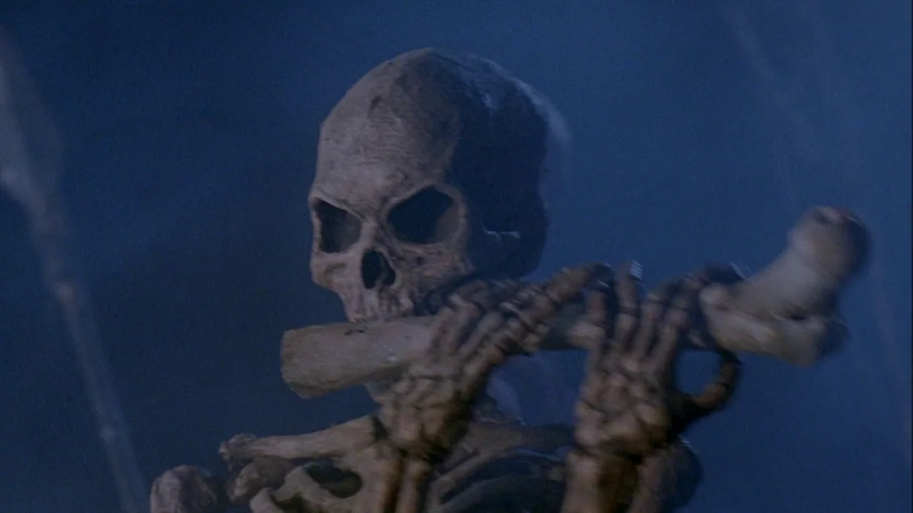 Army of Darkness (1992) movie still: closeup — A skeletal figure stands against a dark, blue-lit background in a nocturnal environment. The skeleton…