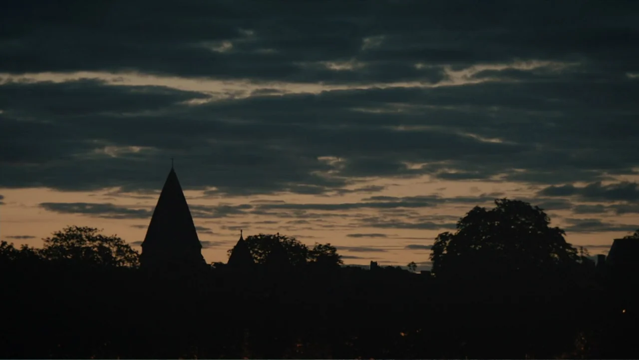 Copenhagen (2002) movie still: establishing — A dark town silhouette rests against a band of orange sunset clouds. The horizon is dominated by sharp…