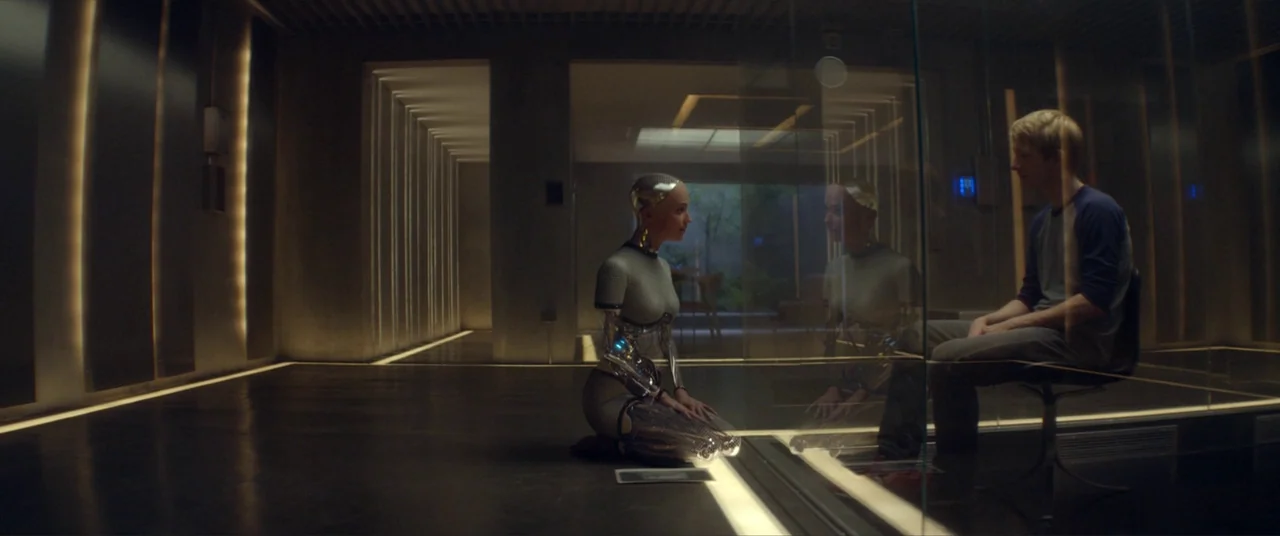 Ex Machina (2015) movie still: wide — A minimalist observation chamber features dark flooring and integrated wall-mounted strip lights. A robotic…