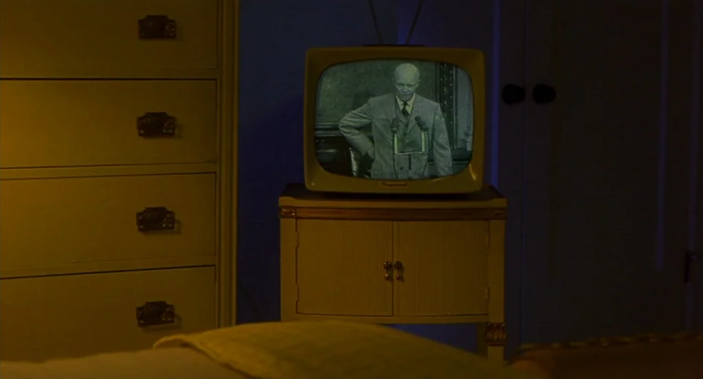 Far From Heaven (2002) movie still: medium — A dimly lit room contains a white dresser and a small cabinet holding a television. The television…