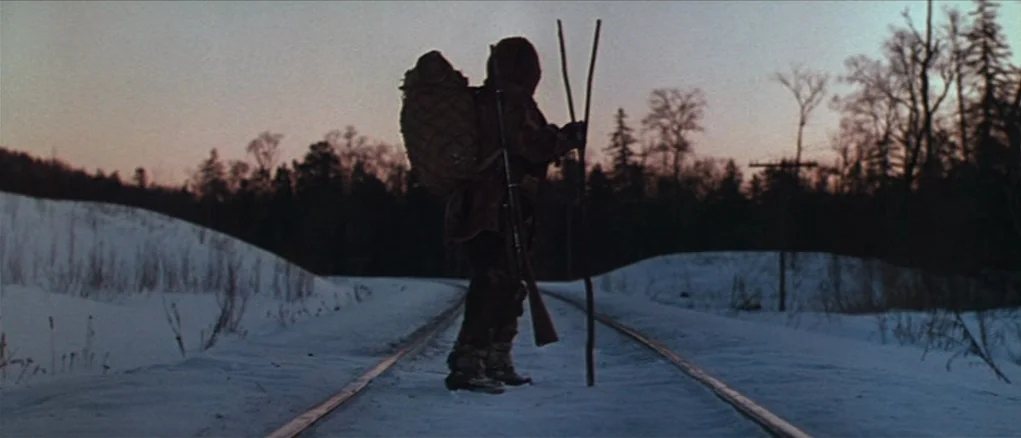 Dersu Uzala (1975) movie still: fullbody — Snow-covered railway tracks stretch through a desolate landscape under a dim winter dusk sky. A lone…