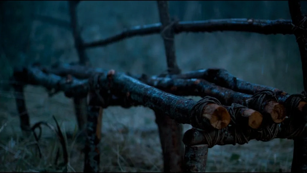 Che Part 2 (Guerrilla) (2008) movie still: medium — A handmade rustic fence constructed from dark, wet branches sits in a field. Thin rain falls…
