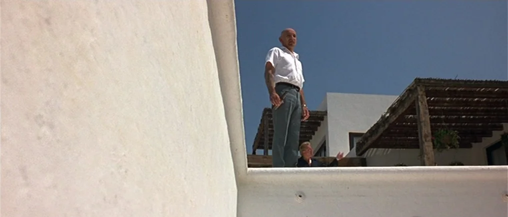 Sexy Beast (2000) movie still: fullbody — A Mediterranean villa exterior features stark white walls and wooden pergola structures overhead. A bald…