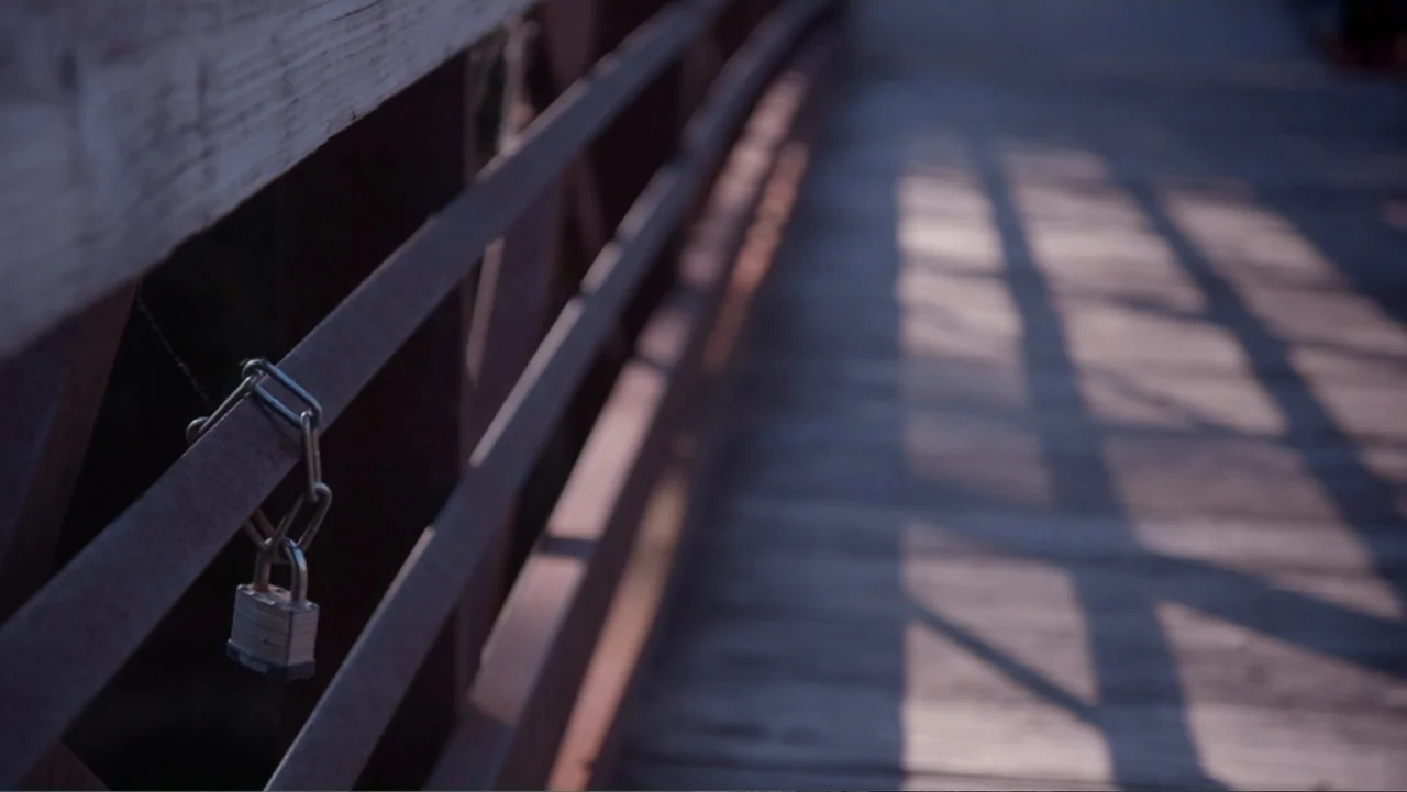 Beware the Slenderman (2016) movie still: closeup — A wooden pedestrian bridge features a metal railing with a single hanging padlock. The late…