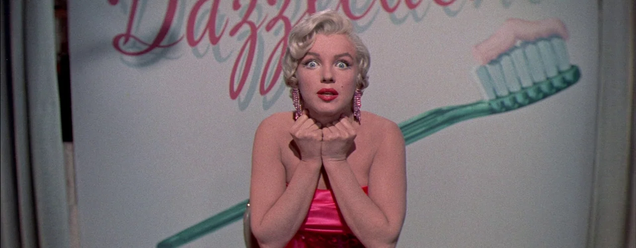 The Seven Year Itch (1955) movie still: medium — A light-colored backdrop features a large graphic illustration of a toothbrush with toothpaste. A…