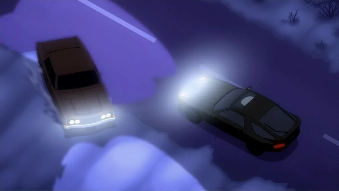 Batman: Year One (2011) movie still: wide — An asphalt road at night stretches through a darkened, rural area under moonlight. Two automobiles…