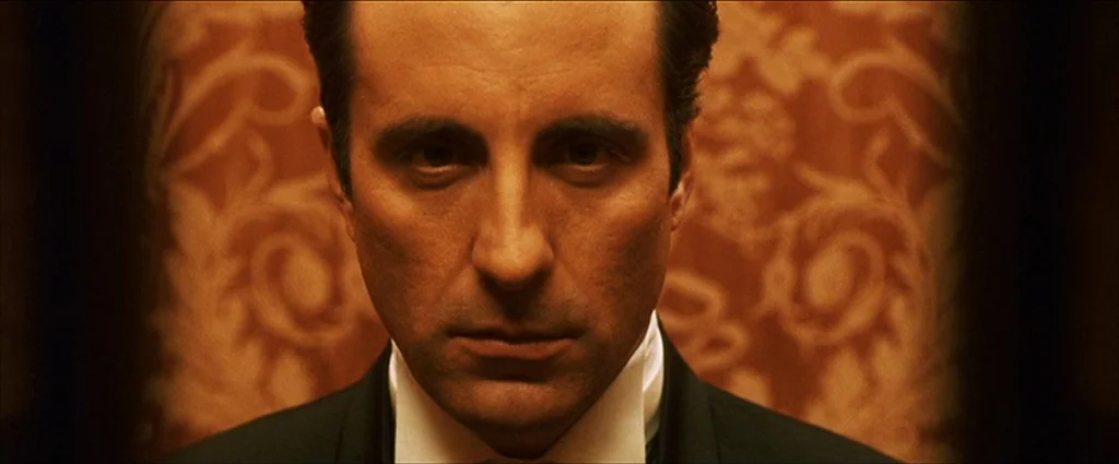 Ocean’s Eleven (2001) movie still: closeup — A man stands centered against a decorative orange wallpaper background with ornate patterned textures.…