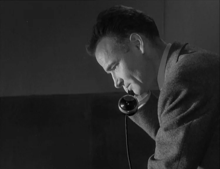 Bob le Flambeur (1956) movie still: medium — A dark indoor space with minimal background detail visible in monochromatic tones. A man in a wool suit…