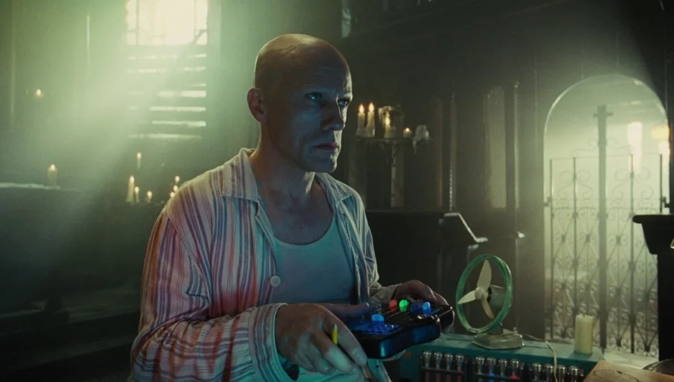 The Zero Theorem (2013) movie still: medium — A dark, moody chapel interior filled with dust motes and soft light rays. A bald man wearing pajamas…