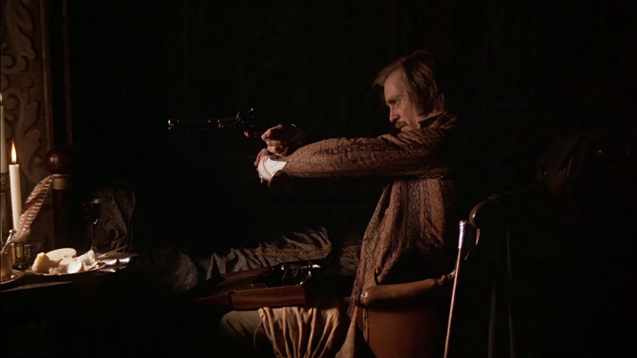 The Duellists (1977) movie still: medium — A dimly lit room contains a set table with a burning candle. A man sits at the table, aiming a pistol…
