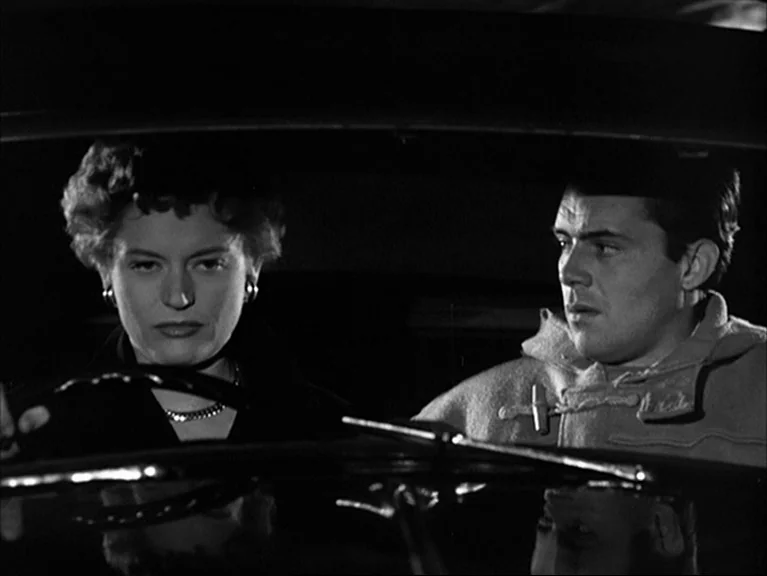 The Sleeping Tiger (1954) movie still: medium — The interior of a vehicle at night with two people sitting side by side. A woman holds the steering…