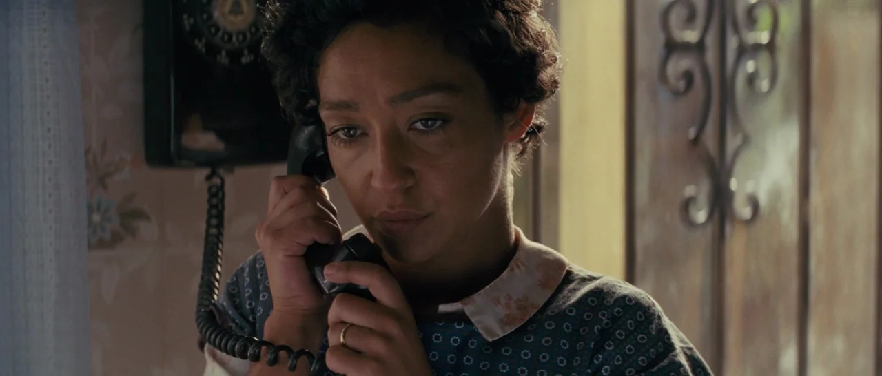 Loving (2016) movie still: closeup — A woman stands in a dimly lit domestic hallway with patterned wall covering. She holds a black vintage…