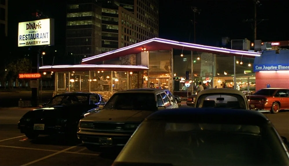 The Limey (1999) movie still: establishing — A roadside diner with a signature mid-century modern peaked roof and neon trim. Several parked vehicles…