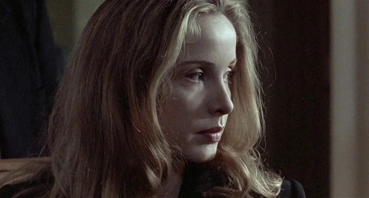 Three Colours: White (1994) movie still: closeup — A dimly lit indoor space with blurred background details. The woman with blonde hair turns her…
