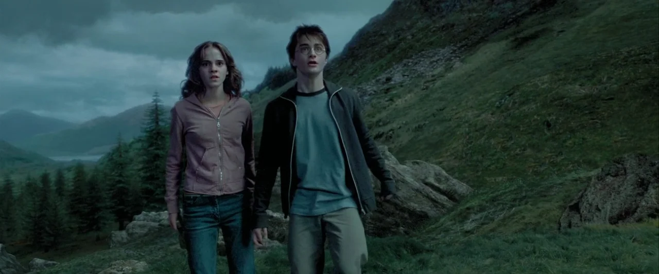 Harry Potter and the Prisoner of Azkaban (2004) movie still: fullbody — A green mountain slope with rocky outcrops and pine trees under overcast…