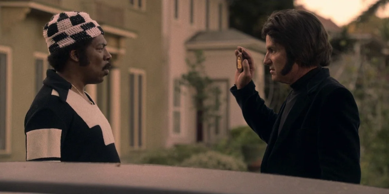 Dolemite Is My Name movie still: medium — Two men stand outdoors on a quiet residential street with houses in the background. A man in a blazer…