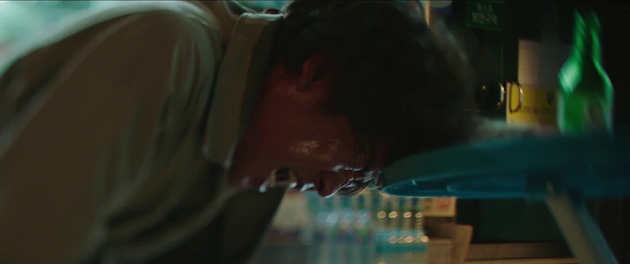 Psychokinesis (2018) movie still: closeup — A dimly lit convenience store aisle with blurred merchandise shelves visible in the background. A man…
