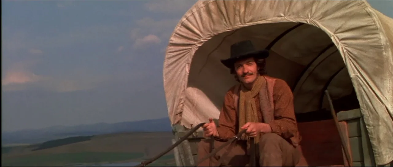 Ravenous (1999) movie still: medium — A man sits inside the front of a canvas-covered wagon on a grassy plain. He holds the reins as the wagon…