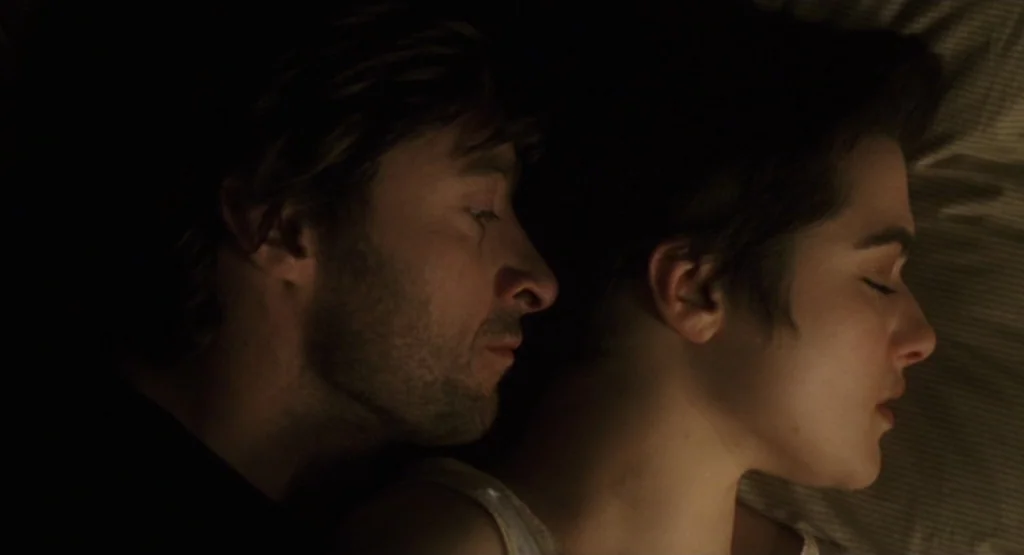 The Fountain (2006) movie still: closeup — A man and a woman lie in bed side by side in a dimly lit space. They both have their eyes closed while…
