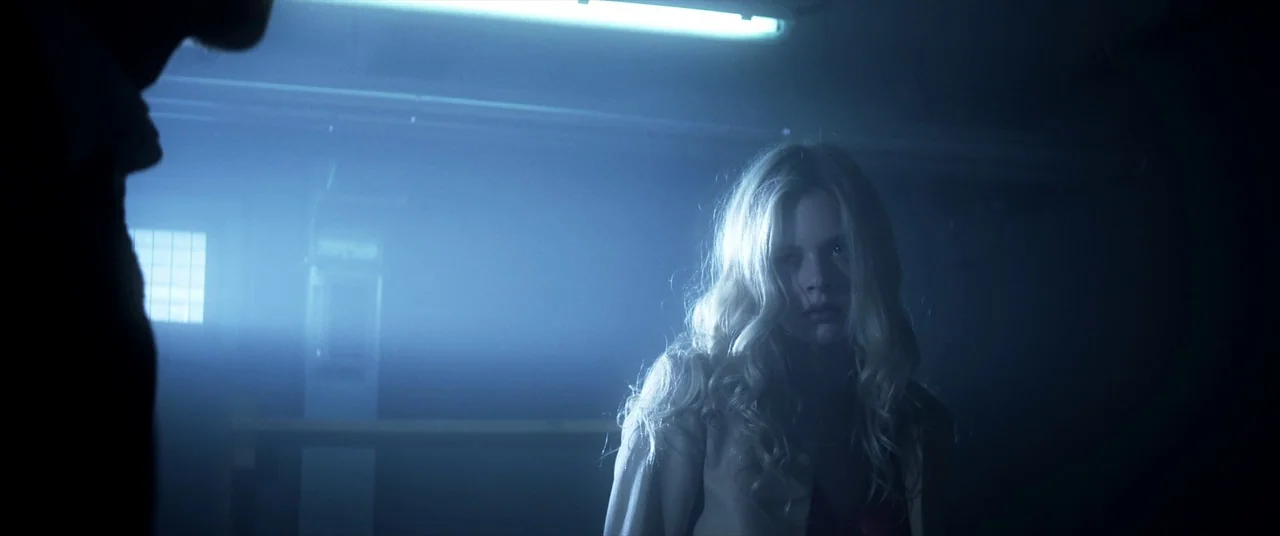 Mayhem (2017) movie still: medium — A dark, windowless basement is illuminated by a single flickering overhead fluorescent light fixture. A young…