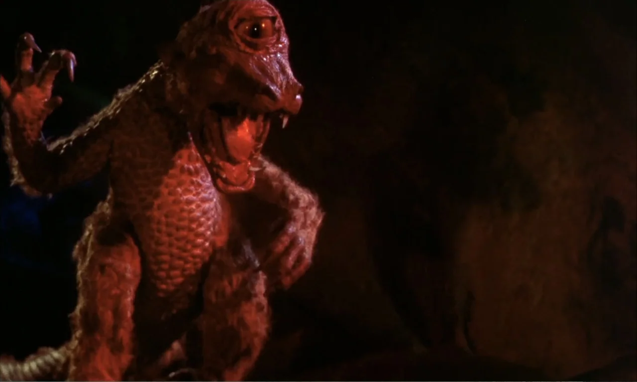 Journey to the Seventh Planet (1962) movie still: medium — A dimly lit rock-walled cave interior provides the setting for a monstrous encounter. A…