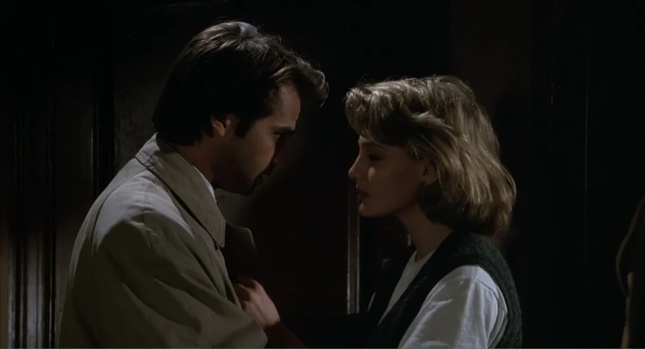 I, Madman (1989) movie still: medium — A dimly lit interior space with dark walls and minimal environmental detail. A man and a woman stand close to…