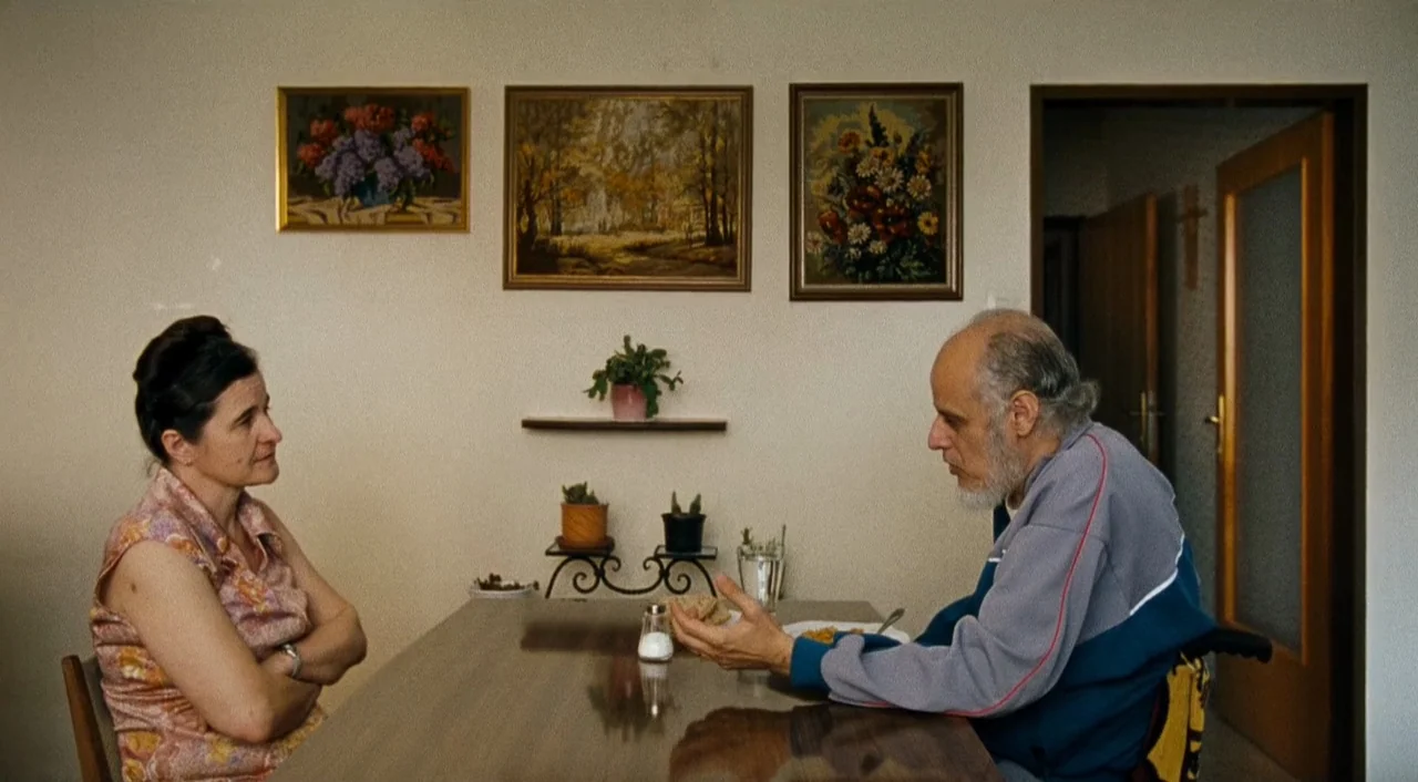 Paradise: Faith (2012) movie still: medium — A plain interior with beige walls decorated by three small framed paintings above a table. A man seated…
