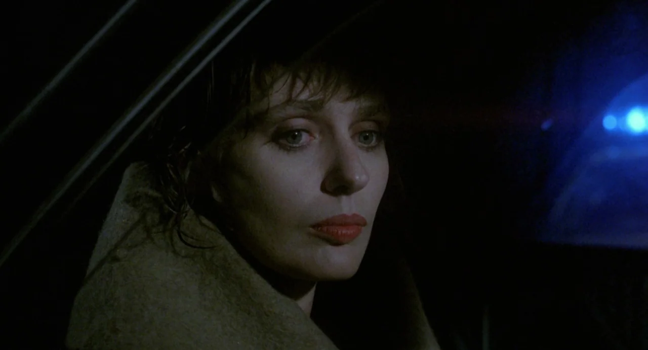StageFright (1987) movie still: closeup — A woman sits inside a car at night with shadows obscuring most of the cabin. She stares out the side…