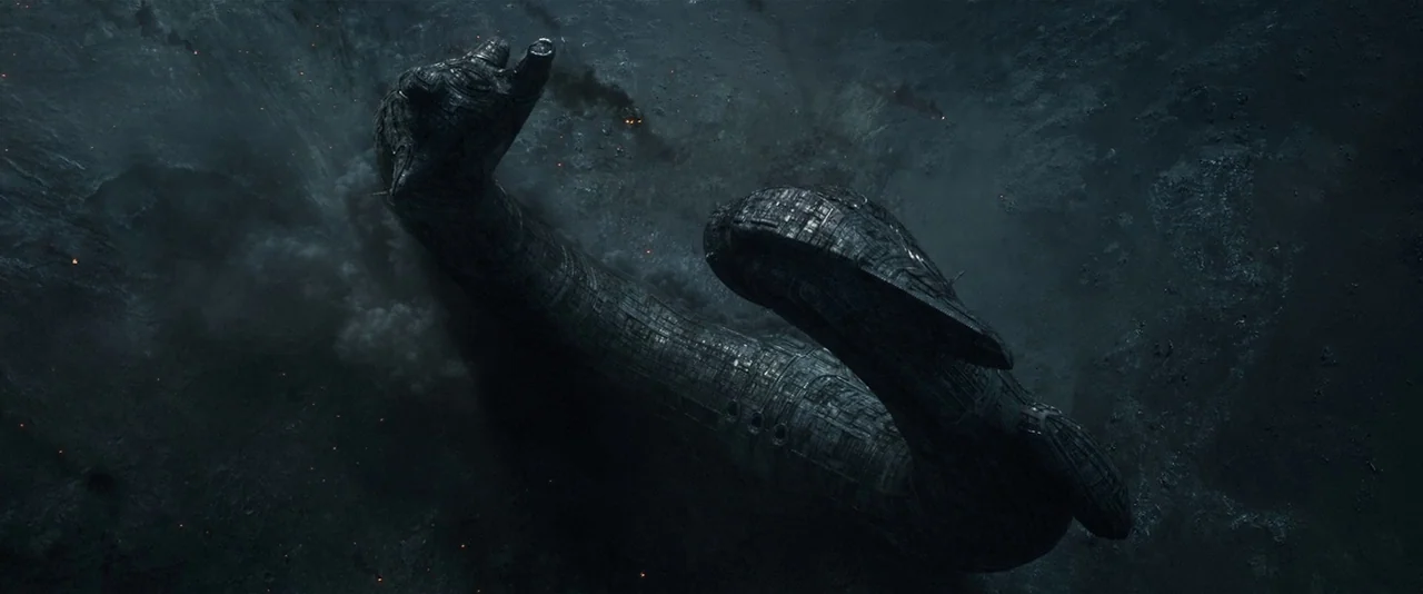 Prometheus (2012) movie still: establishing — A dark, curved alien spacecraft lies embedded in a barren, rocky crater surface. Smoke and debris…