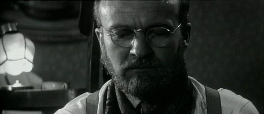And The Fifth Horseman is Fear (1965) movie still: closeup — A dimly lit indoor space featuring a man seated near a warm light source. The man is…