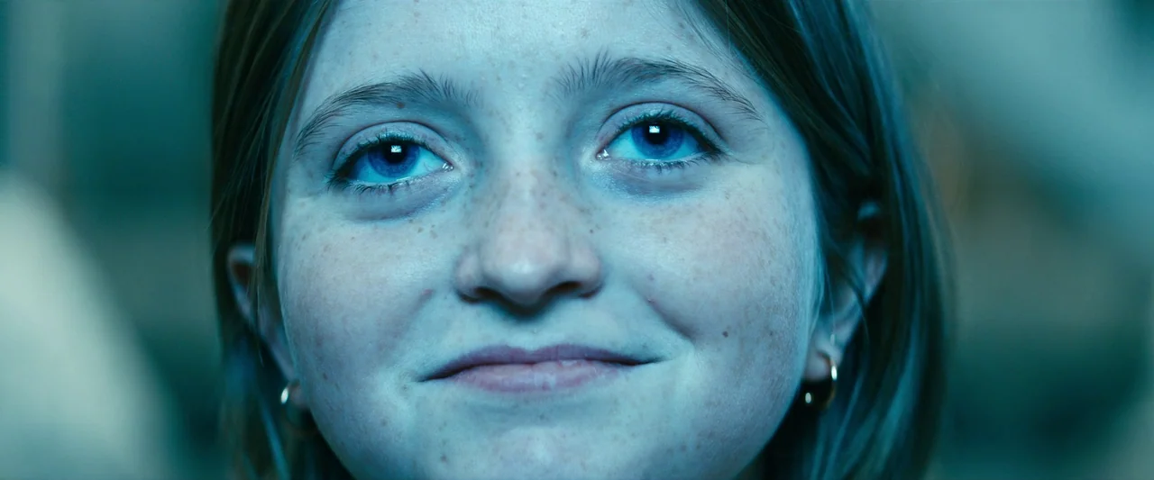 Leave The World Behind (2023) movie still: closeup — A close-up shot focuses on a young woman's face within a dark interior space. She stares ahead…
