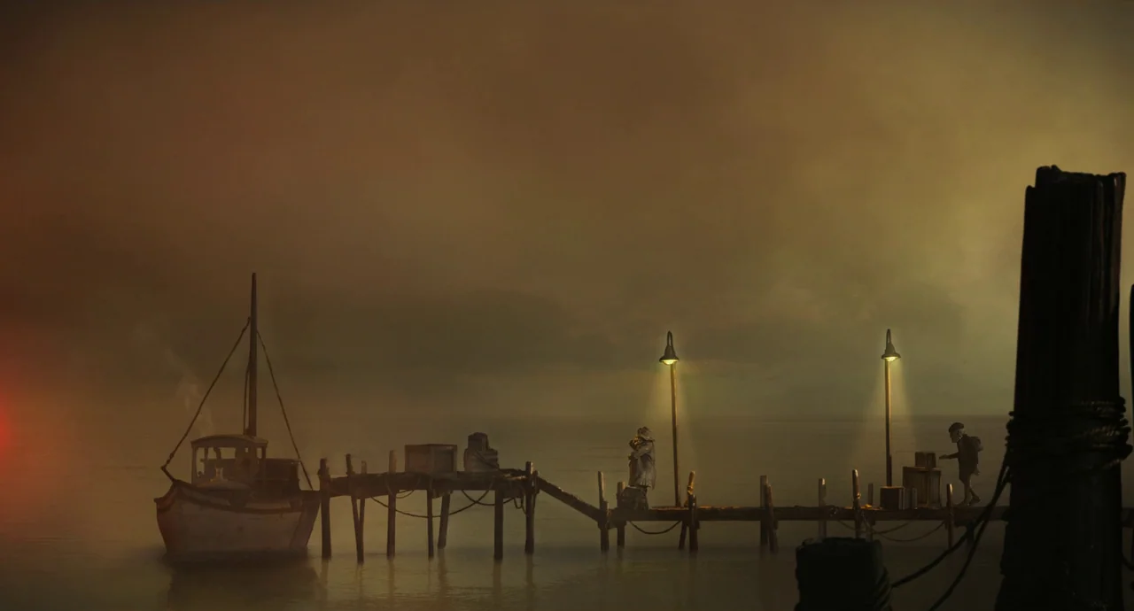Guillermo del Toro’s Pinocchio (2022) movie still: wide — A wooden pier extends into calm, dark water under a thick, hazy overcast sky. Two figures…