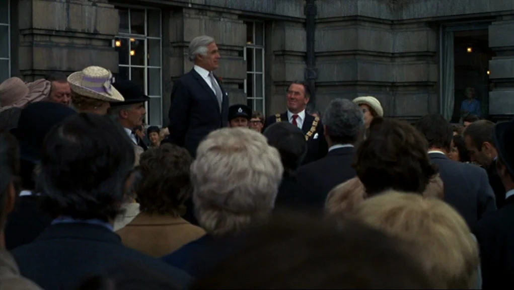 Frenzy (1972) movie still: medium — A stone courtyard with large multi-paned windows fronts an institutional building of classical architecture. An…