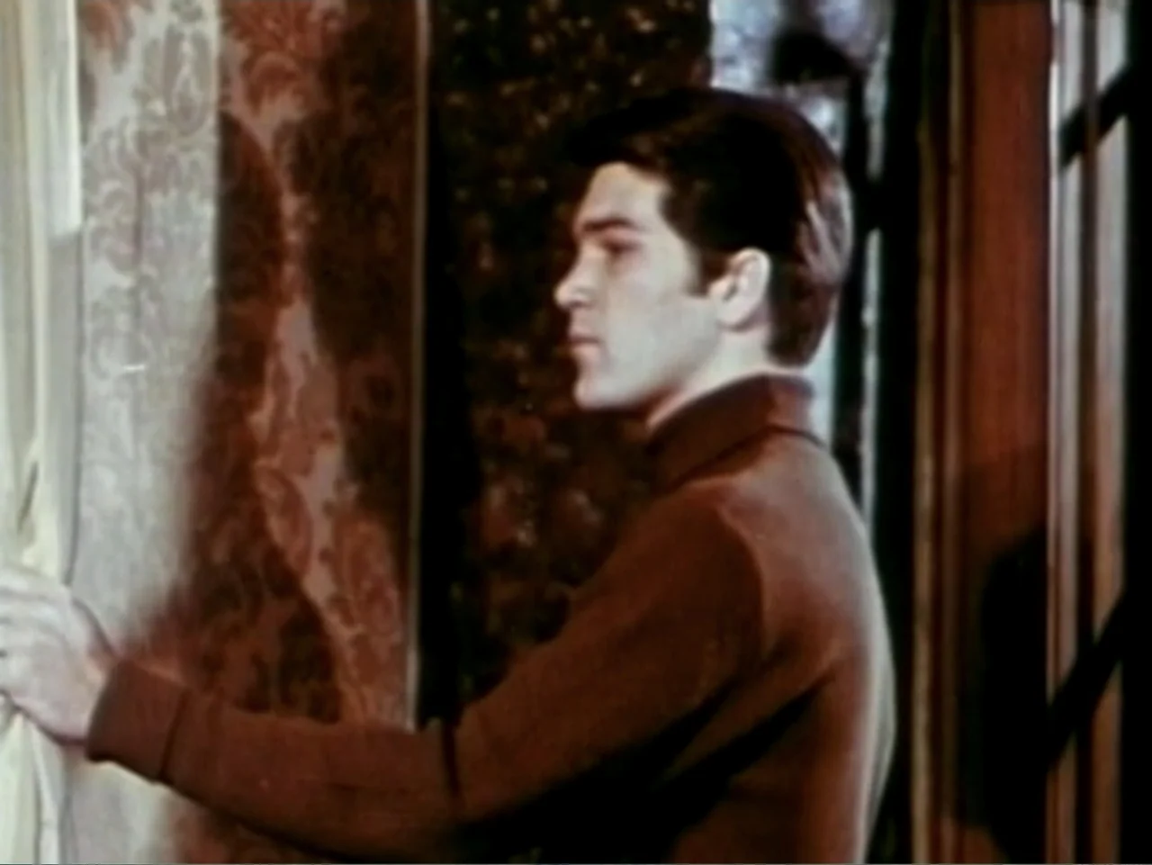 In the Year 2889 (1969) movie still: medium — An interior space features patterned wallpaper and dark wood trim near a window. A young man in a…