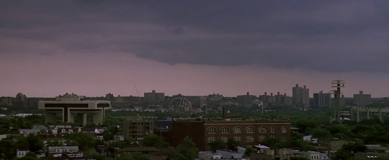 The Yards (2000) movie still: establishing — An aerial panoramic view of a city neighborhood under a heavy purple storm sky. Landmarks including the…
