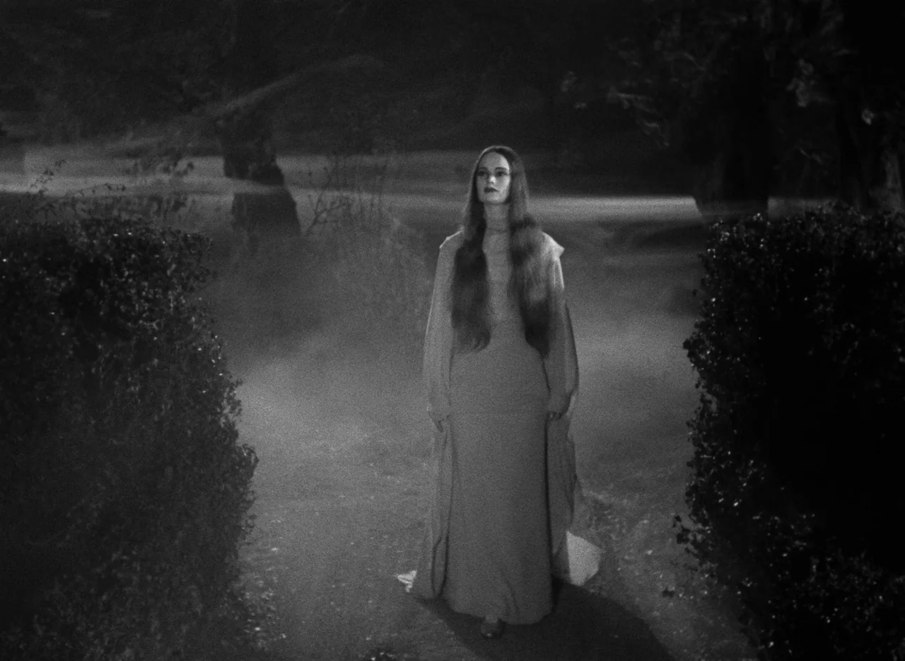 Mark of the Vampire (1935) movie still: fullbody — A woman walks down a dirt path flanked by dark, dense foliage at night. Fog low to the ground…