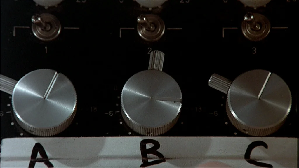 The Conversation (1974) movie still: closeup — Close-up of a black sound mixing console with silver brushed metal knobs. Three large knobs are…