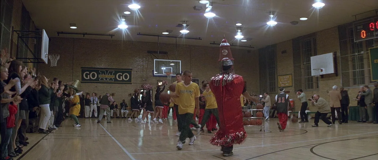 Finding Forrester (2000) movie still: wide — A crowded high school gymnasium features brick walls, basketball hoops, and a scoreboard. Students and…