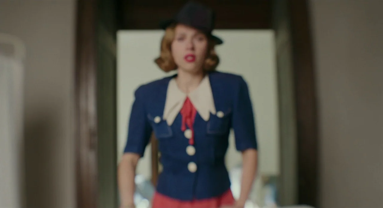 Jojo Rabbit (2019) movie still: medium — A woman stands in a dimly lit hallway wearing a 1940s style outfit. She walks forward through an open…