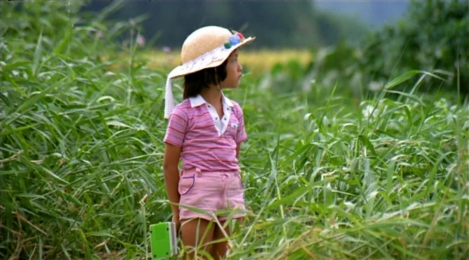 A Summer at Grandpa’s (1984) movie still: medium — A young child stands within a dense patch of tall green grassy vegetation. The child wearing a…