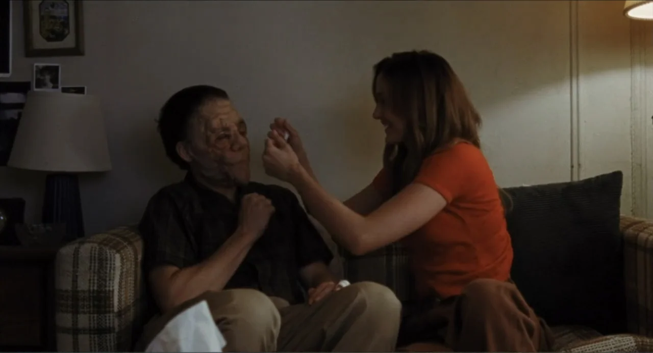 A Different Man (2024) movie still: medium — A domestic space features a patterned sofa placed against a plain light-colored wall. A young woman…