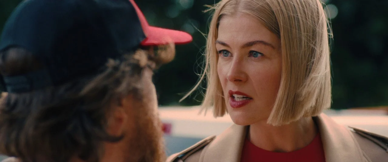 I Care A Lot (2020) movie still: medium — A woman with blonde hair stands outside during the day. She addresses a man wearing a baseball cap while…